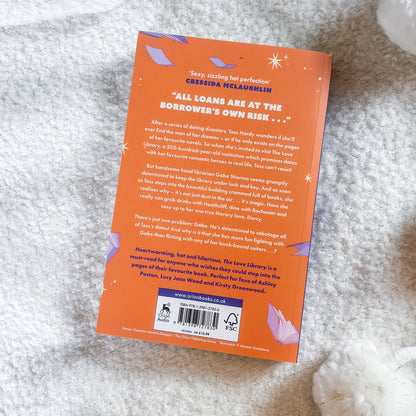 The back cover of an orange paperback book titled 'All Loans are at the Borrower's Own Risk' by Cheerida McLaughlin, placed on a soft white textured blanket.