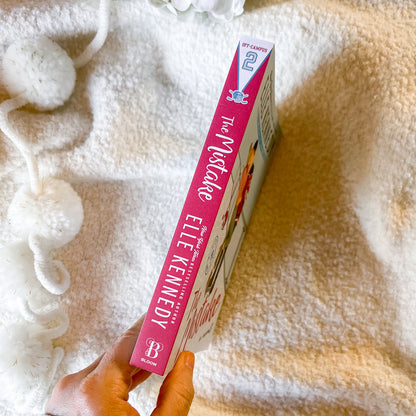 Book titled 'The Mistake' by Elle Kennedy held against a soft, textured background