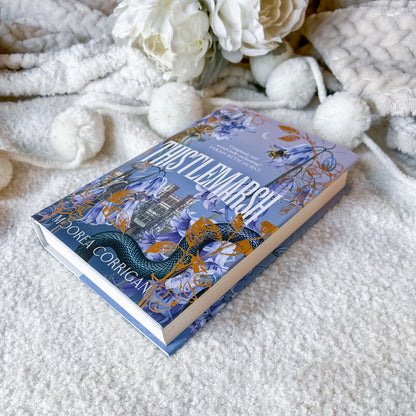 Book titled 'Thistlemarsh' by Andrea Corrigan on a soft white surface with decorative flowers.