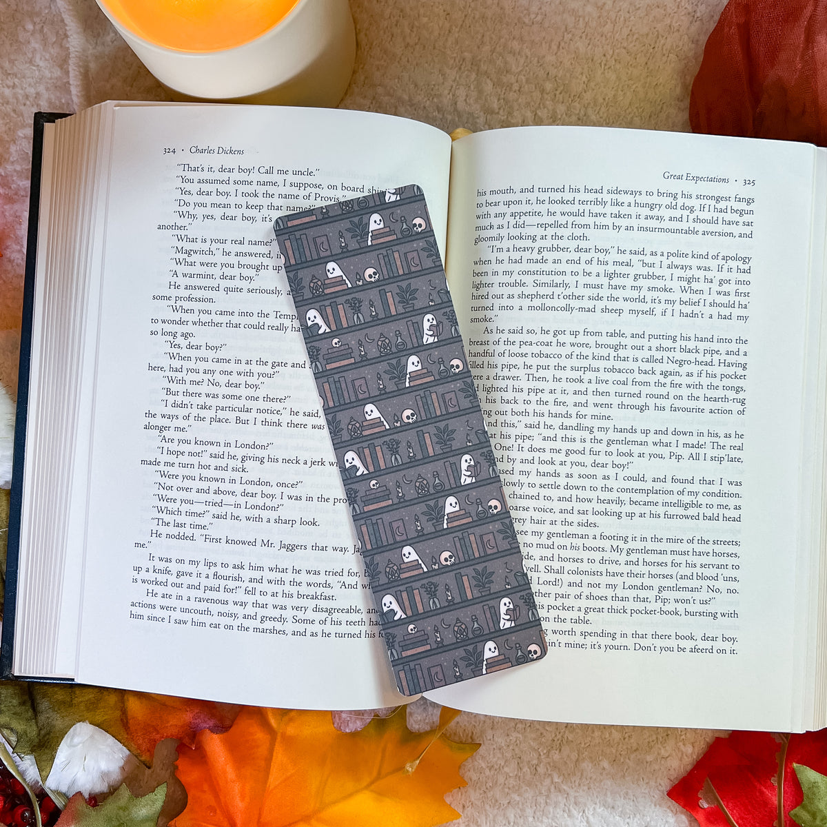 A book open to pages, with a long black bookmark laid across the center. The book is photographed from above on a textured fabric background with small white flowers in the lower left.
