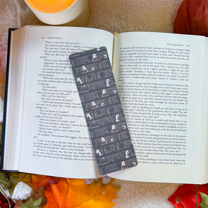 A book open to pages, with a long black bookmark laid across the center. The book is photographed from above on a textured fabric background with small white flowers in the lower left.