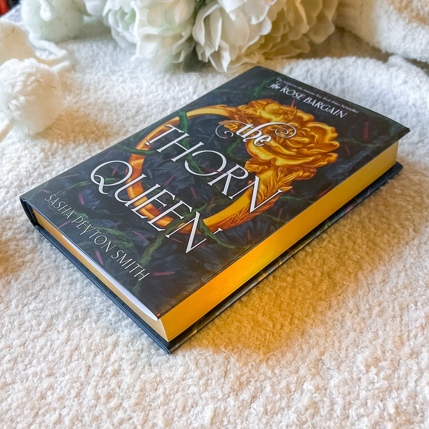 Book titled 'The Thorn Queen' by Sasha Peyton Smith on a textured surface with flowers in the background