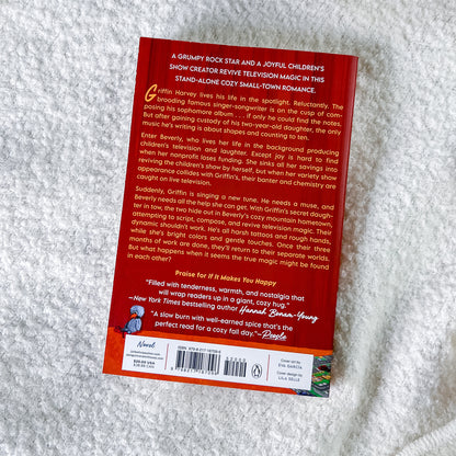 The back cover of the book, photographed flat on a textured white fabric background. The cover features a red-orange background with white text, a small illustration of a boy in a blue sailor outfit, and a small green landscape illustration in the bottom right corner.