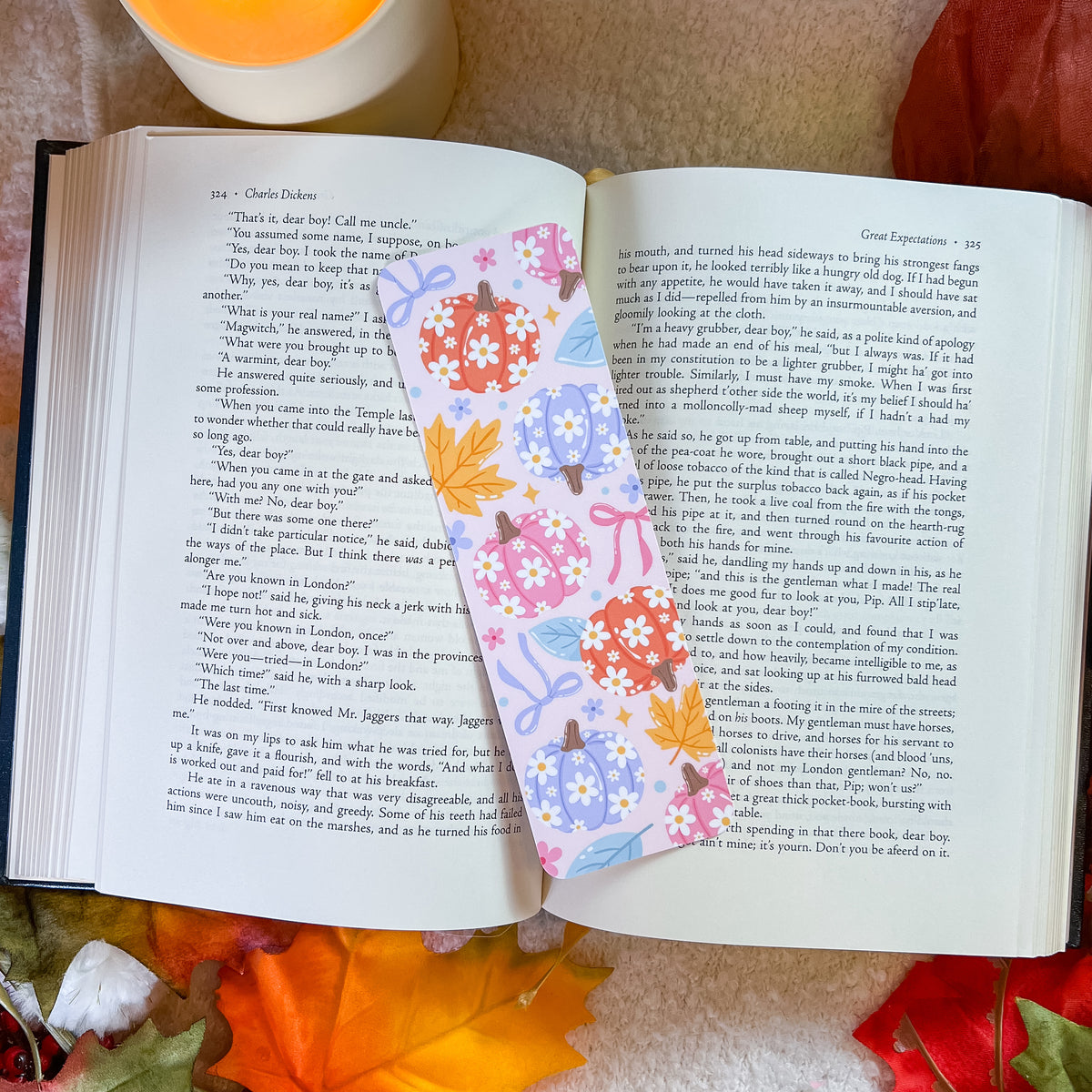 An open book spread laid on a textured orange fabric background, featuring two decorative floral bookmark sheets with colorful illustrations of flowers and butterflies.