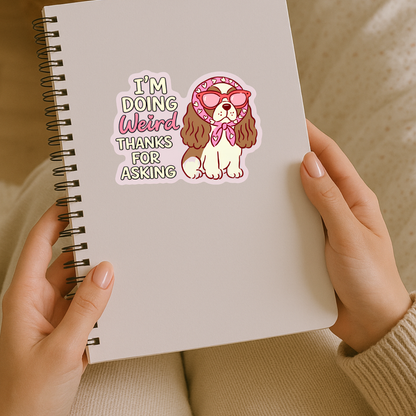 Notebook with a dog sticker and text 'I'm doing weird thanks for asking' held by hands.
