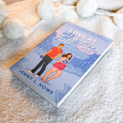 A paperback book titled 'Love at Full Fill' by Jenny L. Howe, featuring a light blue cover with a retro-style illustration of a man and woman, styled on a soft white textured blanket with white pom-pom toys.