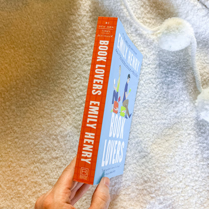 Book titled 'Book Lovers' by Emily Henry held against a textured beige background