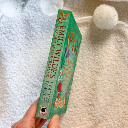 Book titled 'Map of the Otherworld' by Emily Wildes held against a soft, white background.