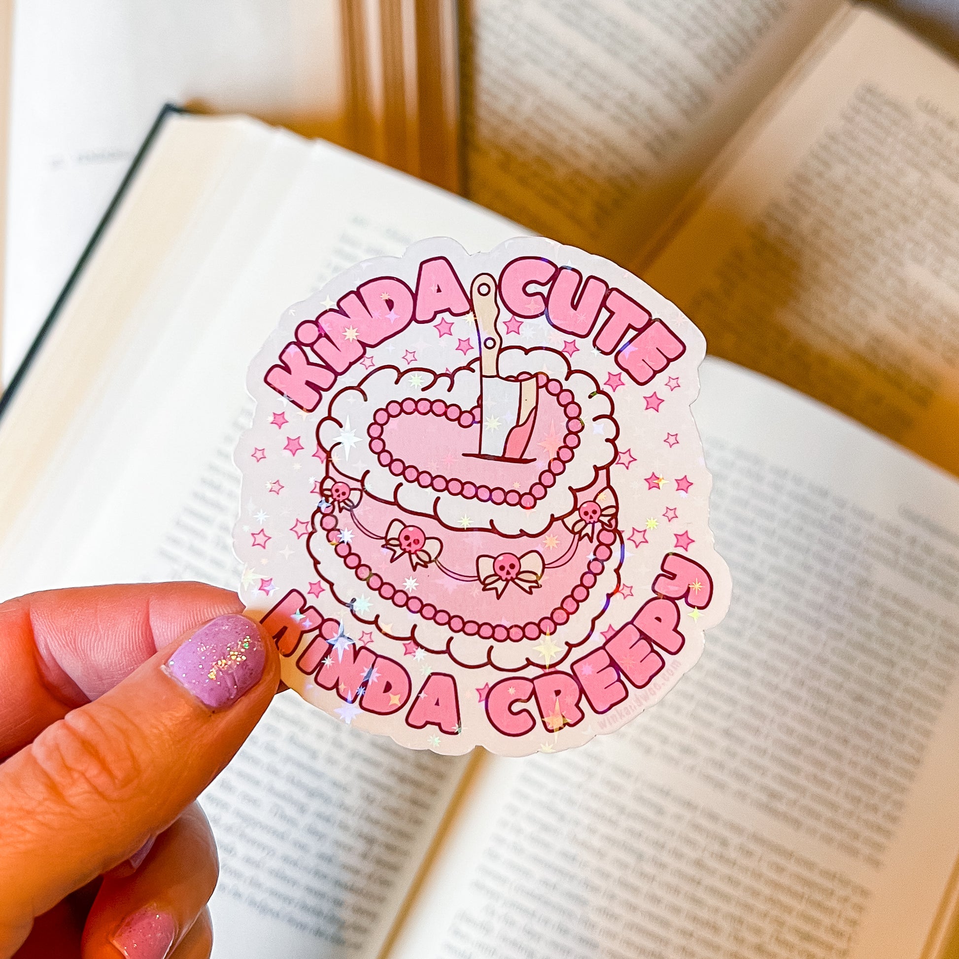 Sticker with 'Kinda Cute Kinda Creepy' text held over an open book