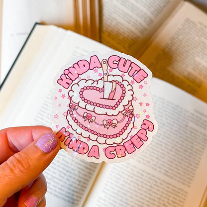 Sticker with 'Kinda Cute Kinda Creepy' text held over an open book