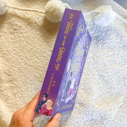 Purple book titled 'throne in the Dark' held against a textured fabric background