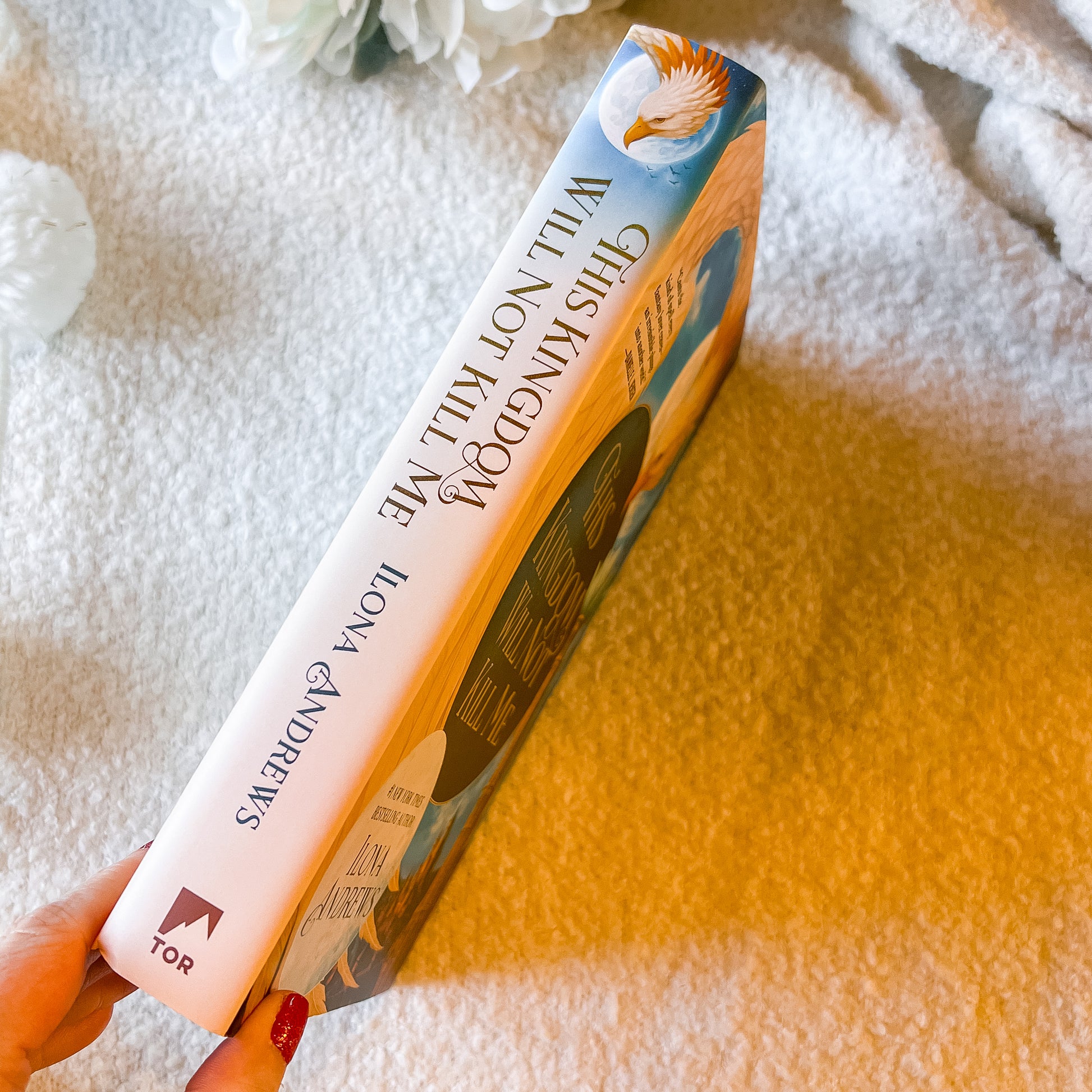 Book titled 'This Kingdom Will Not Kill Me” by Lona Andrews held by a hand on a textured surface.
