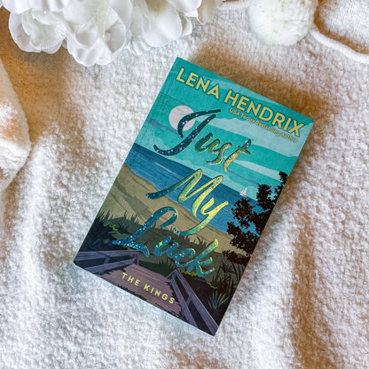 Book titled 'Just My Luck' by Lena Hendrix on a textured surface with flowers.