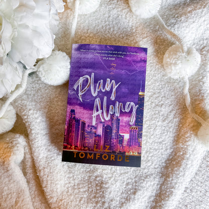Book titled 'Play Along' by Liz Tomforde on a textured surface with floral elements.