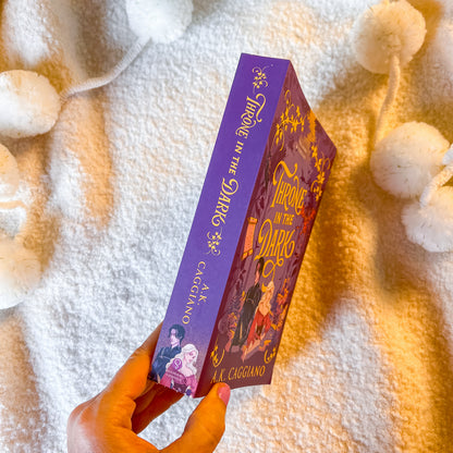 A hand holds a purple book titled 'Throne in the Dark' by A. L.