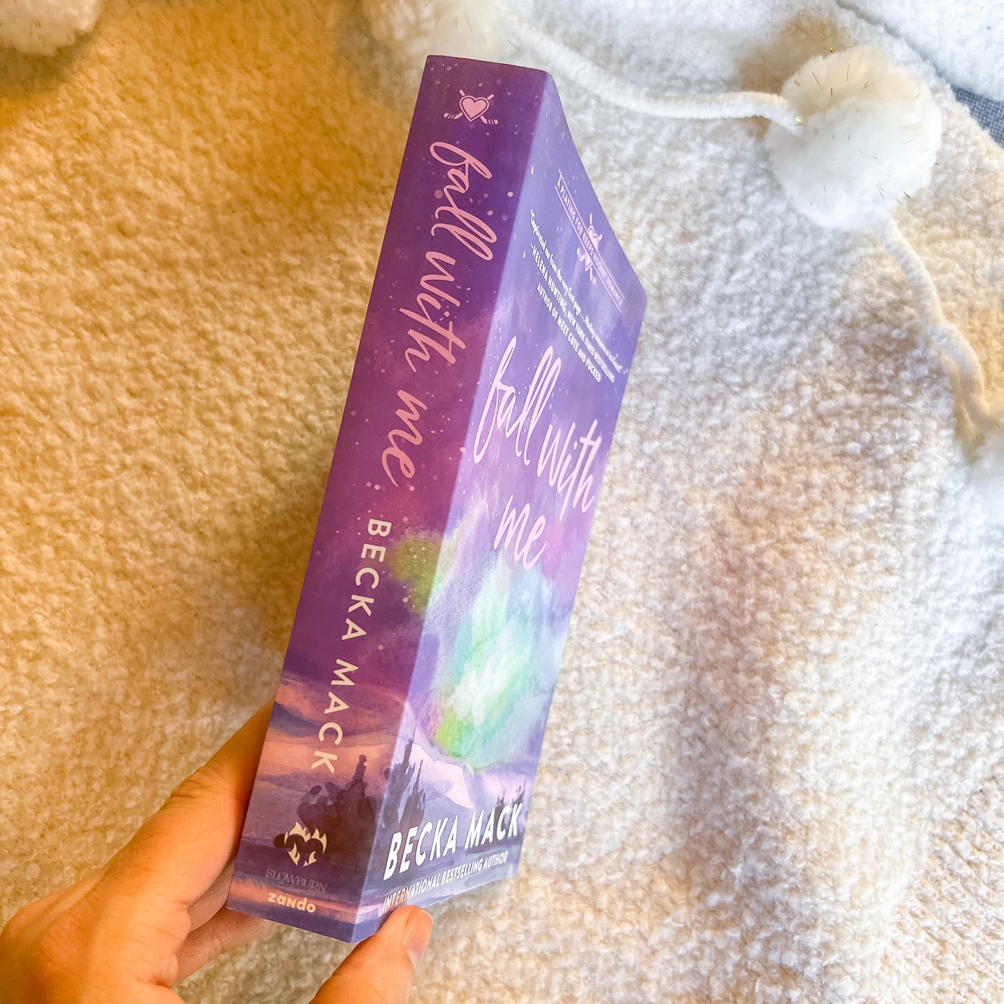 Purple book titled 'Fall with Me' by Becka Mack held against a textured beige background