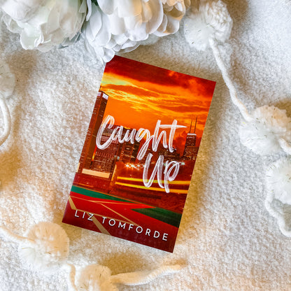 Book titled 'Caught Up' by Liz Tomforde on a textured surface with flowers.