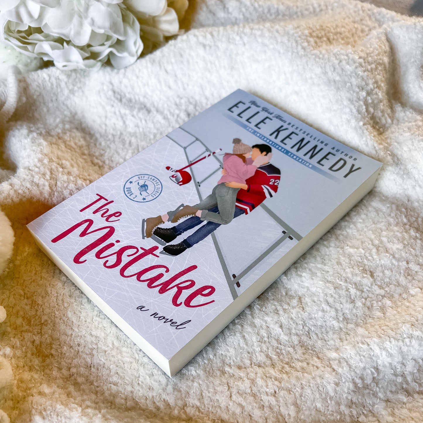 Book titled 'The Mistake' by Elle Kennedy on a soft surface with flowers in the background