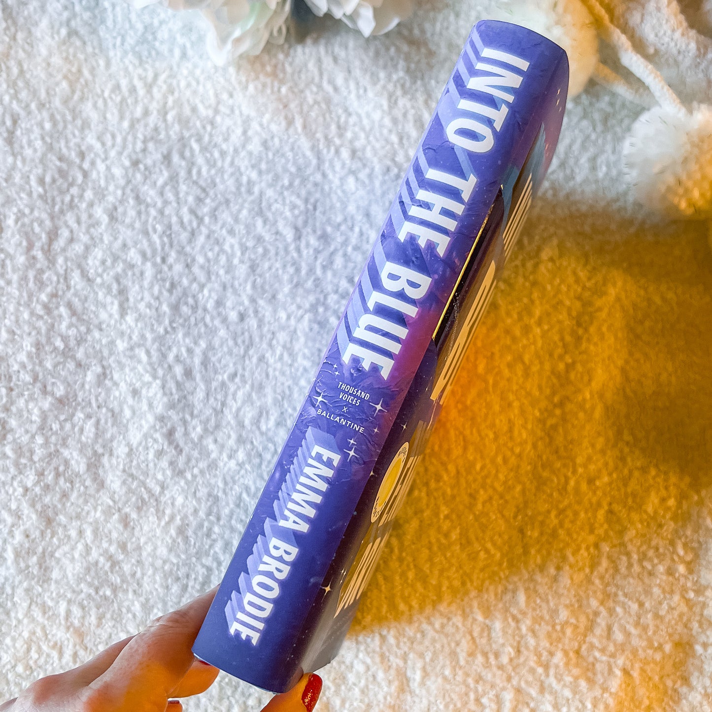 Book with  'Into the Blue' and 'Emma Brodie' text held by a hand on a textured surface.