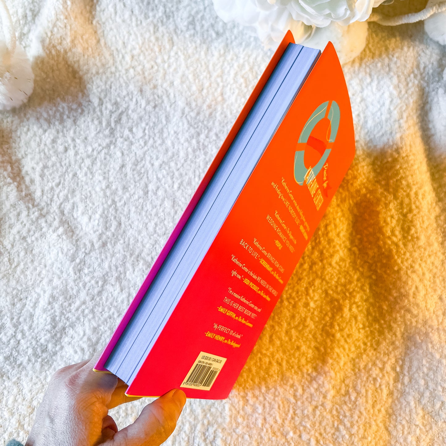Book with a red cover and blue spine held by a hand on a textured white surface.