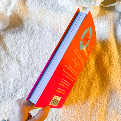Book with a red cover and blue spine held by a hand on a textured white surface.