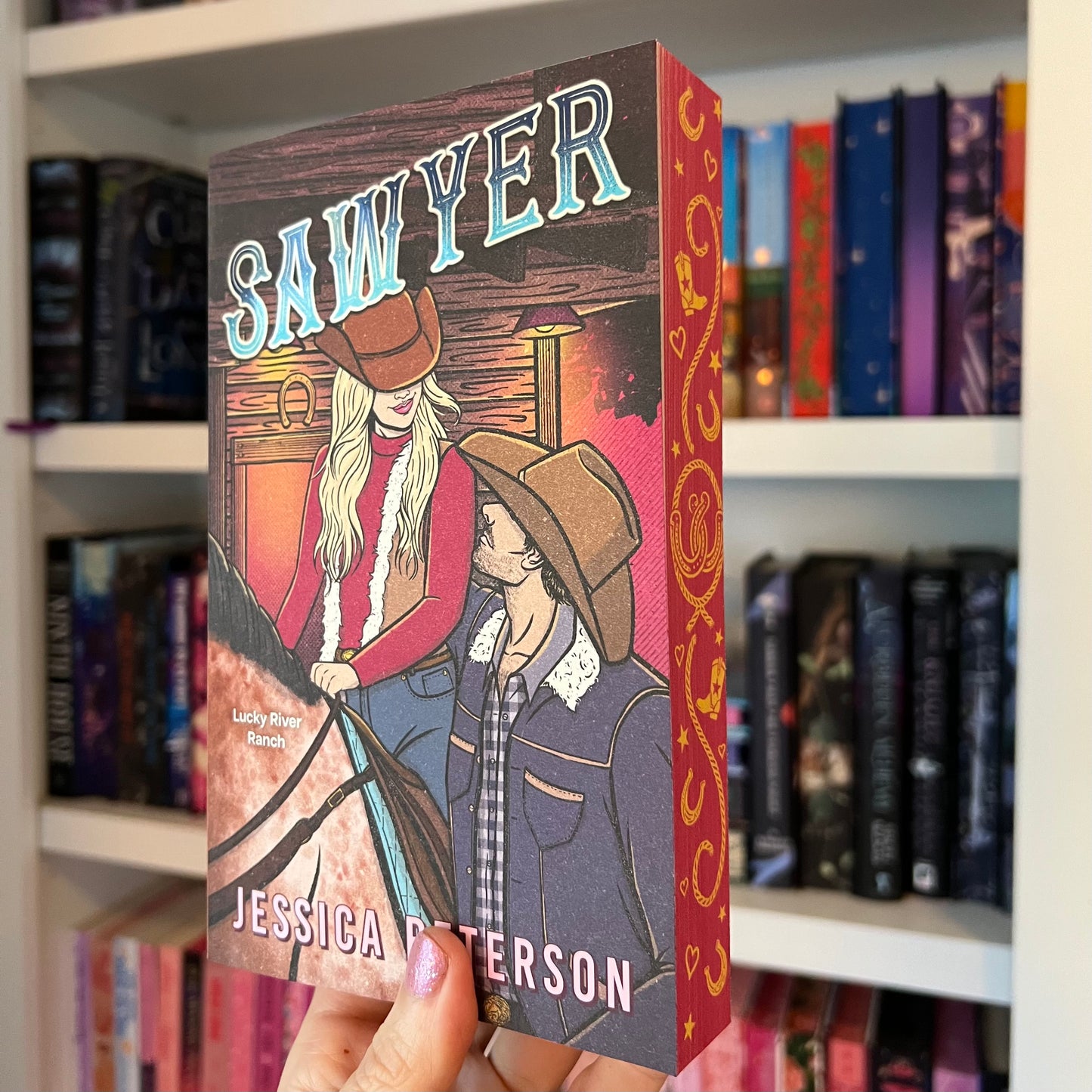 Book titled 'Sawyer' by Jessica Patterson held in front of a bookshelf.