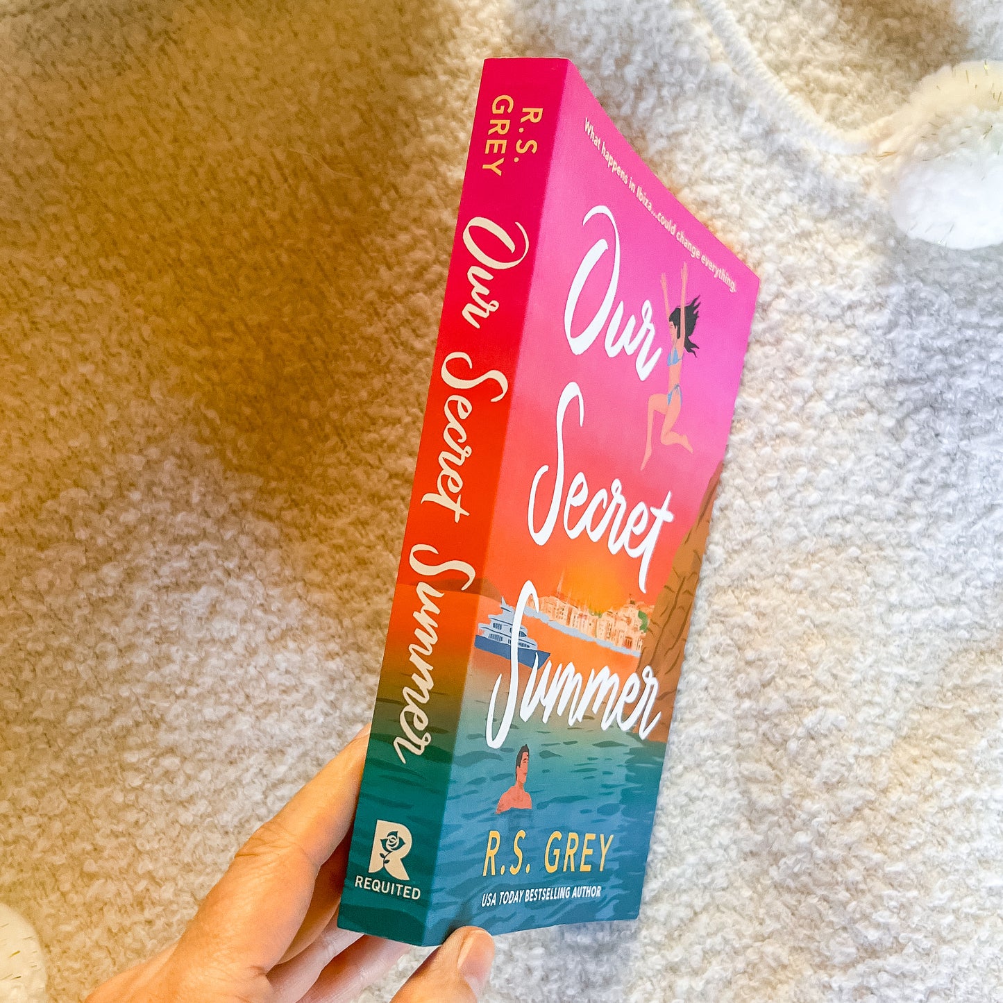 Book titled 'Our Secret Summer' by R.S. Grey held against a textured beige background