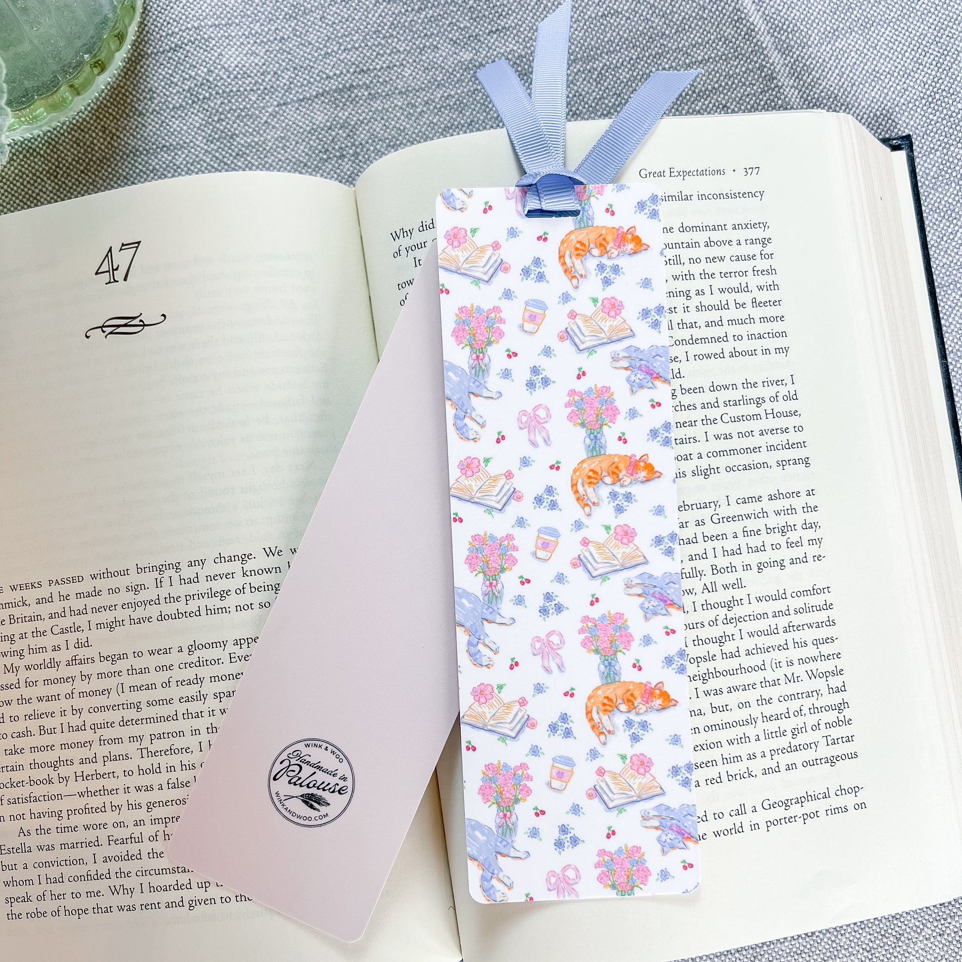 Floral and cat patterned bookmark with a blue ribbon lying on top of a book.