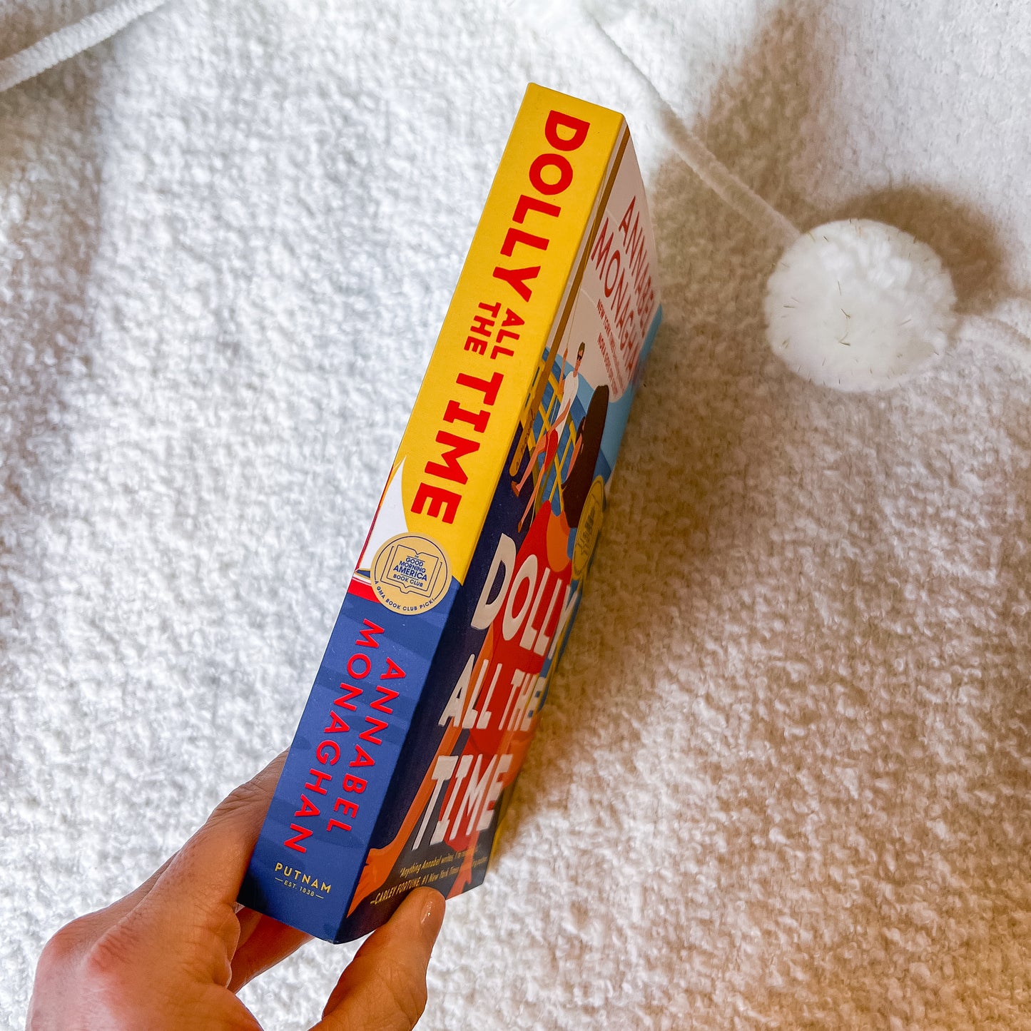 Book titled 'Dolly All the Time' held by a hand on a textured surface