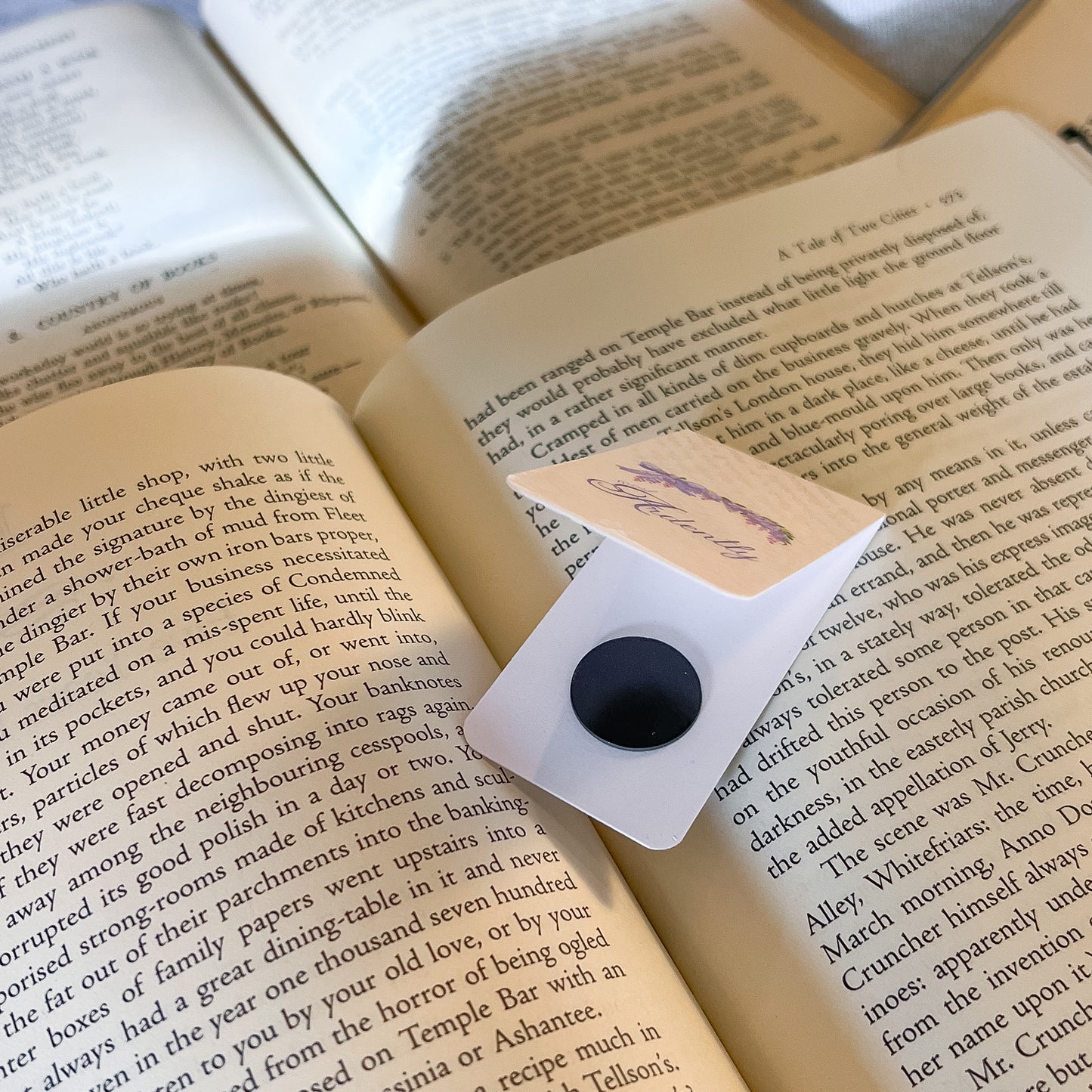 Open book with a bookmark featuring a black button and white card on a wooden surface.