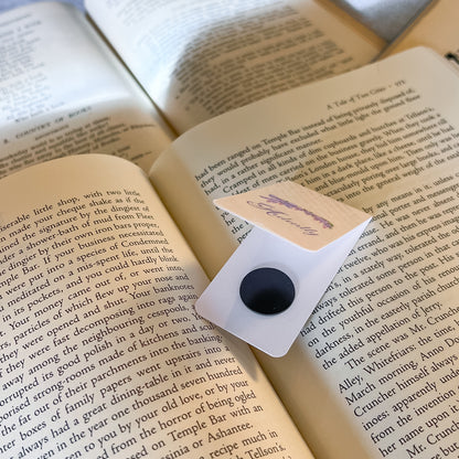 Open book with a bookmark featuring a black button and white card on a wooden surface.