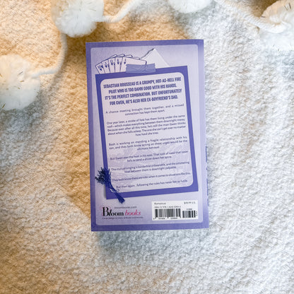 The back cover of a paperback book published by Bloom Books, placed on a soft white textured blanket.