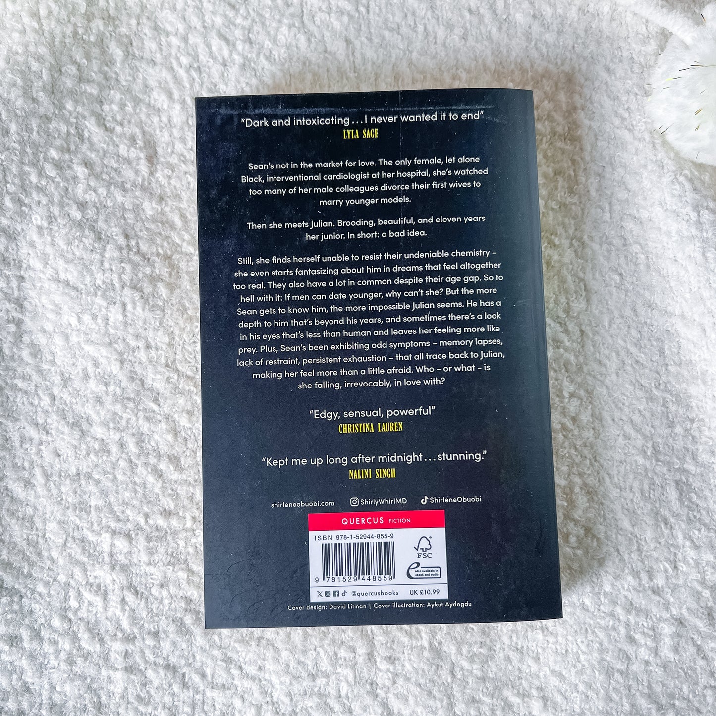 The back cover of the book, featuring a black background with white text, a red 'SUBSCRIBE' banner, and a barcode, photographed on a white textured blanket.