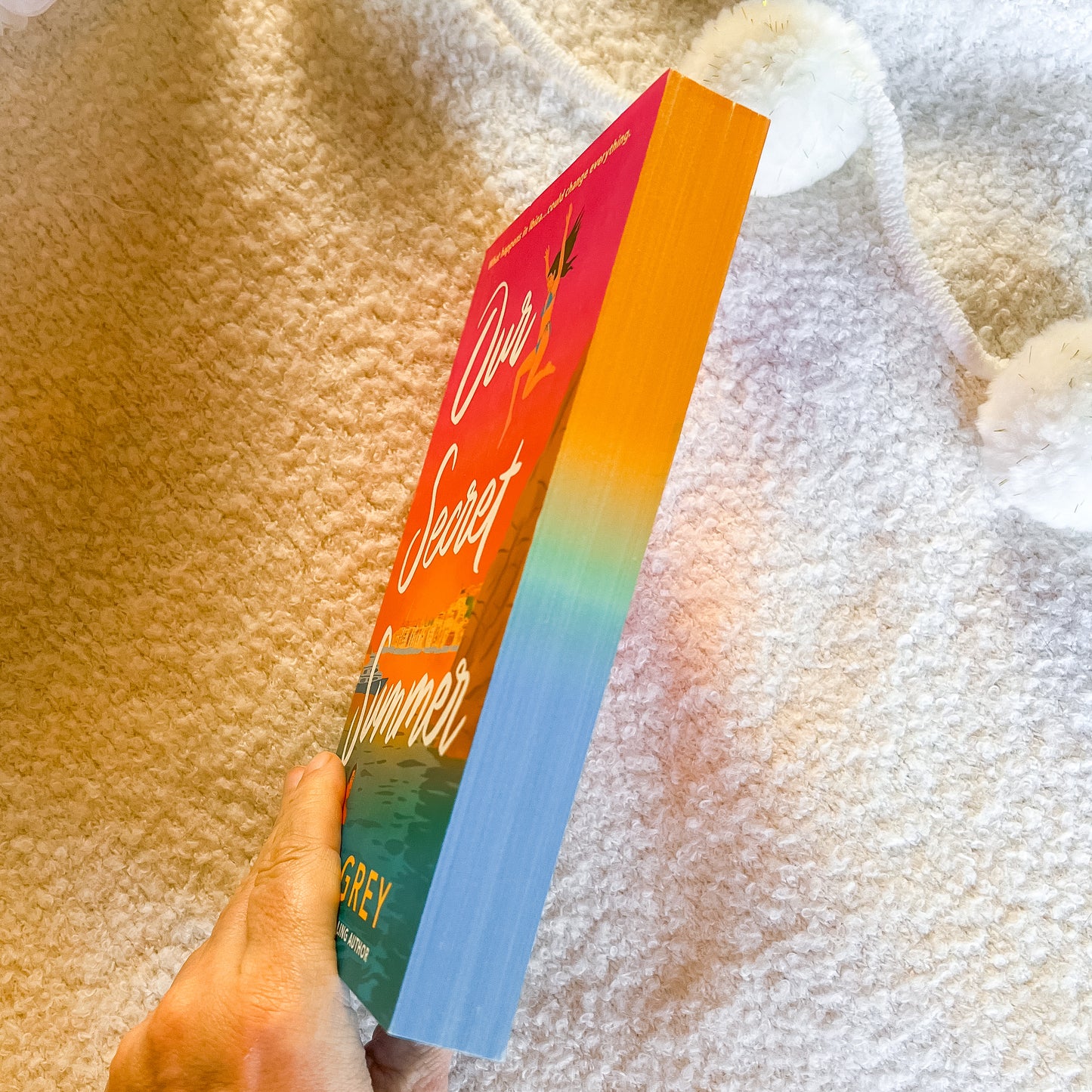 Book titled 'Our Secret Summer' held against a textured fabric background