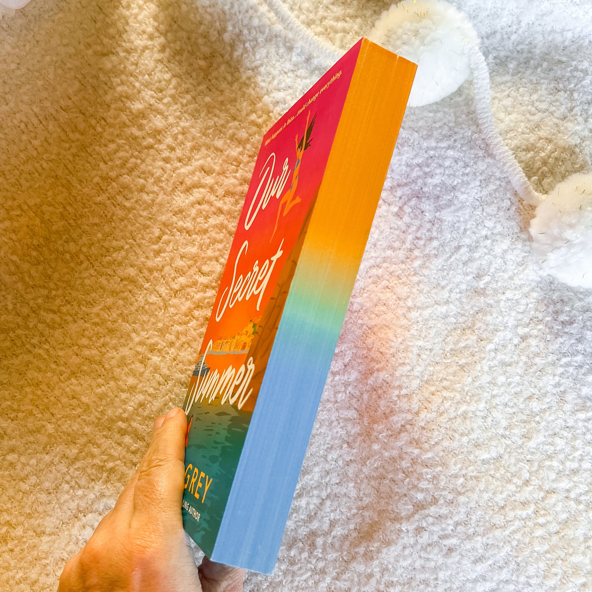 Book titled 'Our Secret Summer' held against a textured fabric background