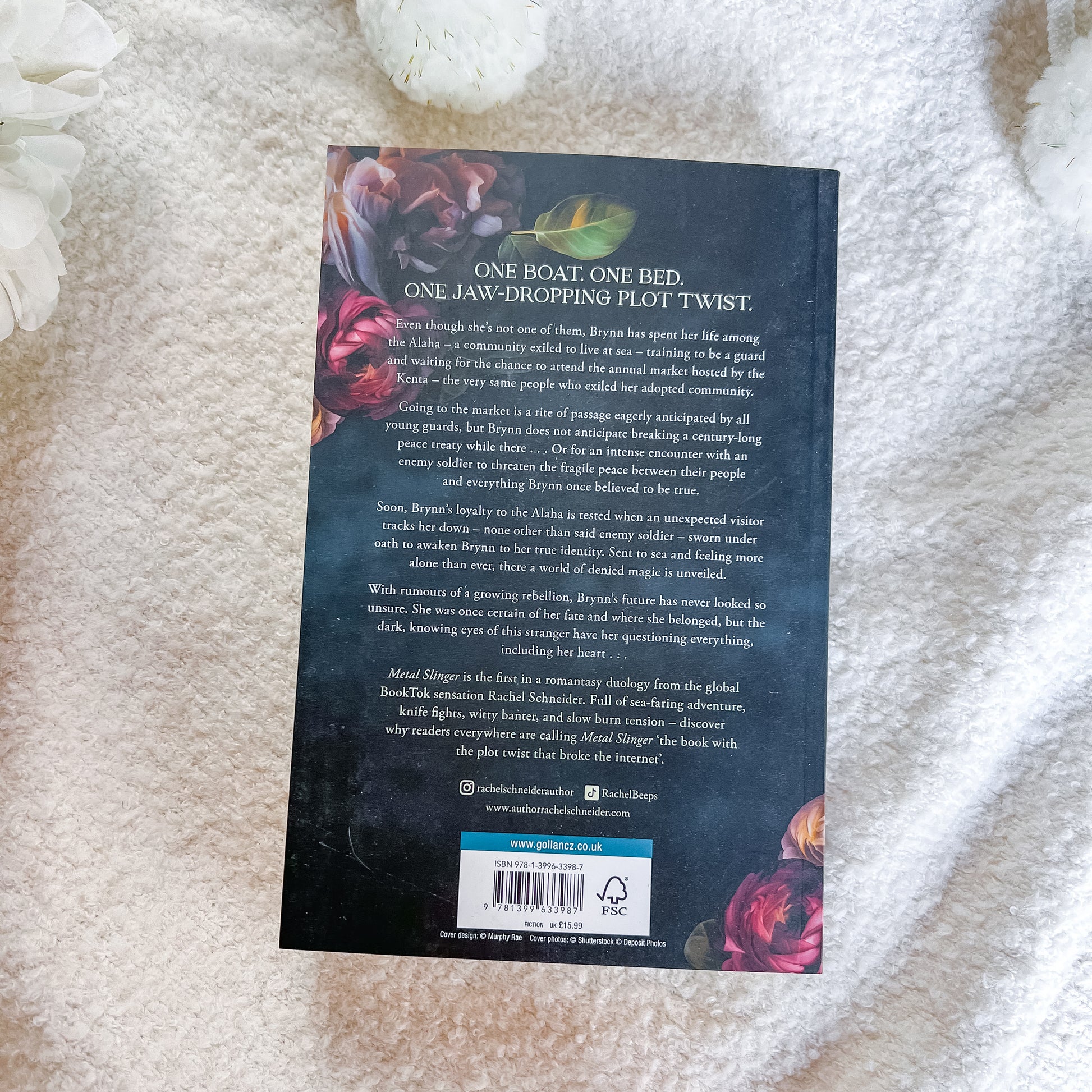 The back cover of the book, displayed flat on a white textured blanket with decorative white flowers in the corners.
