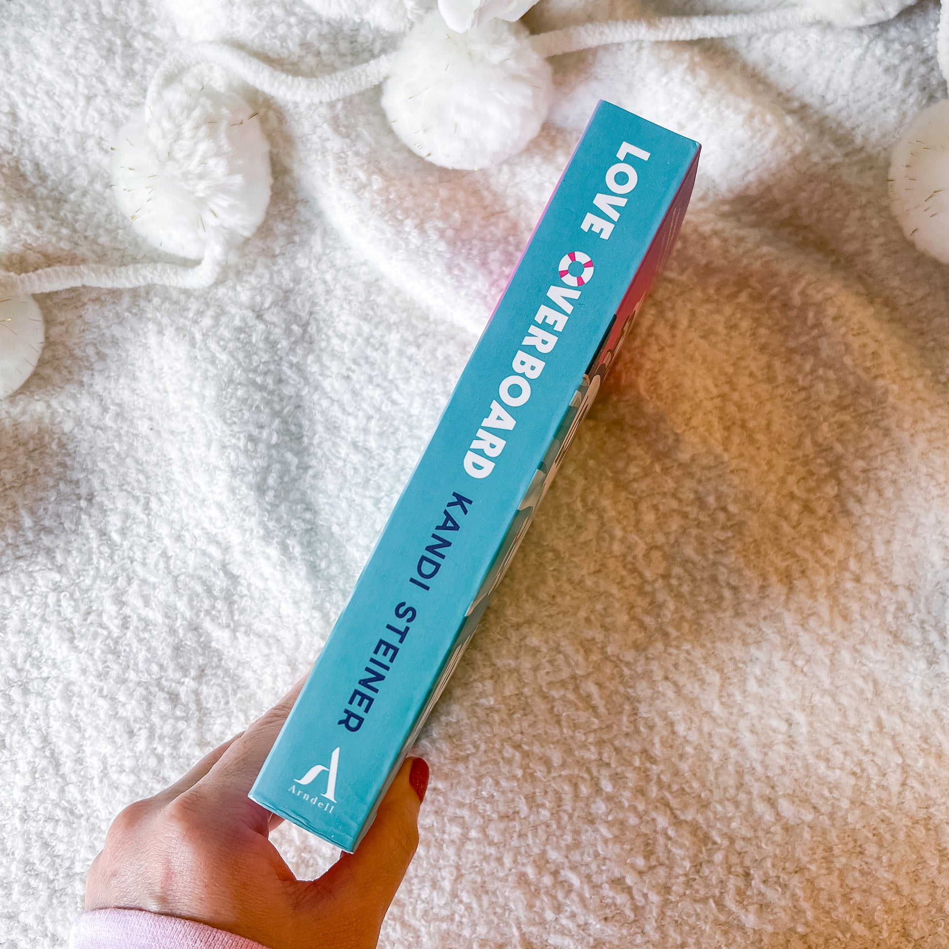 Blue book titled 'Love Over Board' by Kandi Steiner held by a hand on a textured surface.