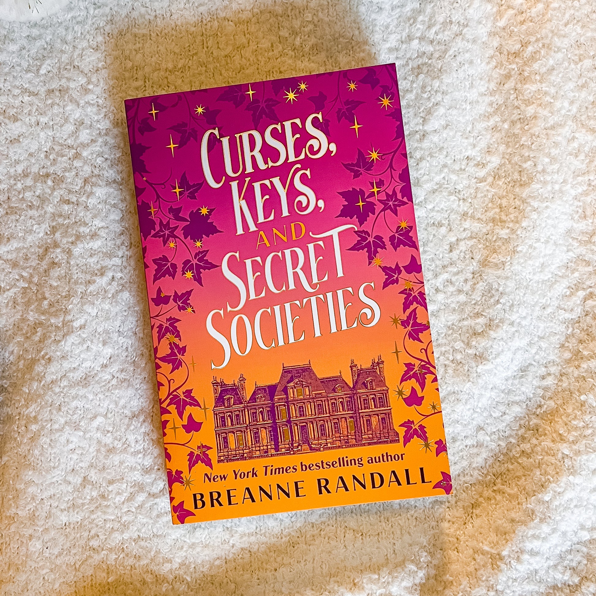 Book titled 'Curses, Keys, and Secret Societies' by Breanne Randall on a textured surface