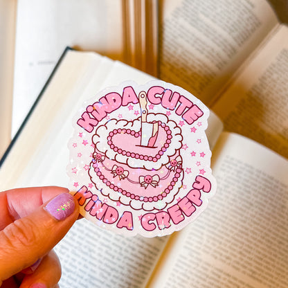 Sticker with 'Kinda Cute Kinda Creepy' text held over an open book