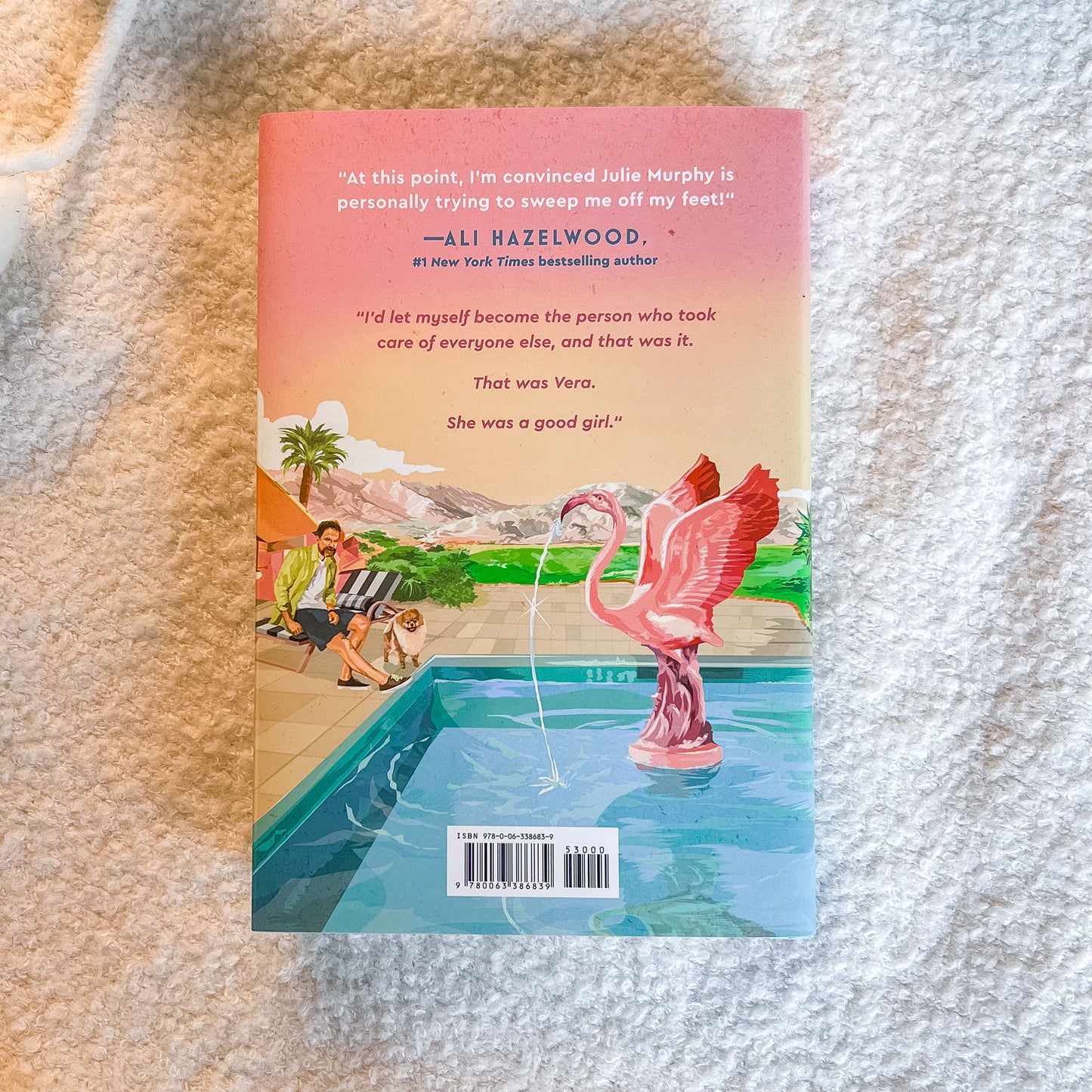 The back cover of the book, featuring a pink flamingo fountain spraying water from a swimming pool, set against a textured white blanket background.