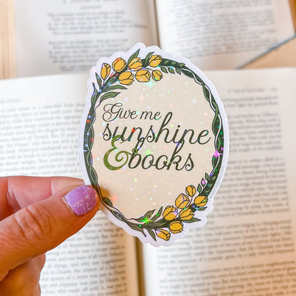 Sticker with 'Give me sunshine and books' text held over an open book