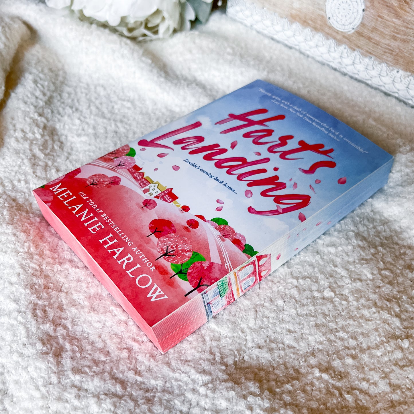 Book titled 'Heart's Landing' by Melanie Harlow on a textured surface with flowers in the background