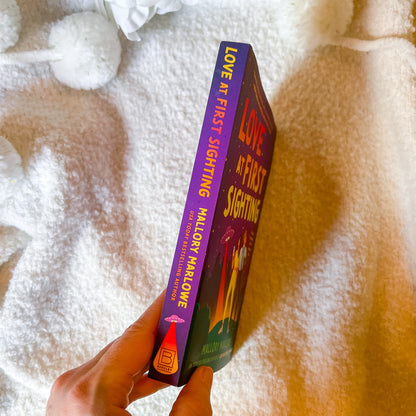 Book titled 'Love at First Sighting' held against a textured white and brown background