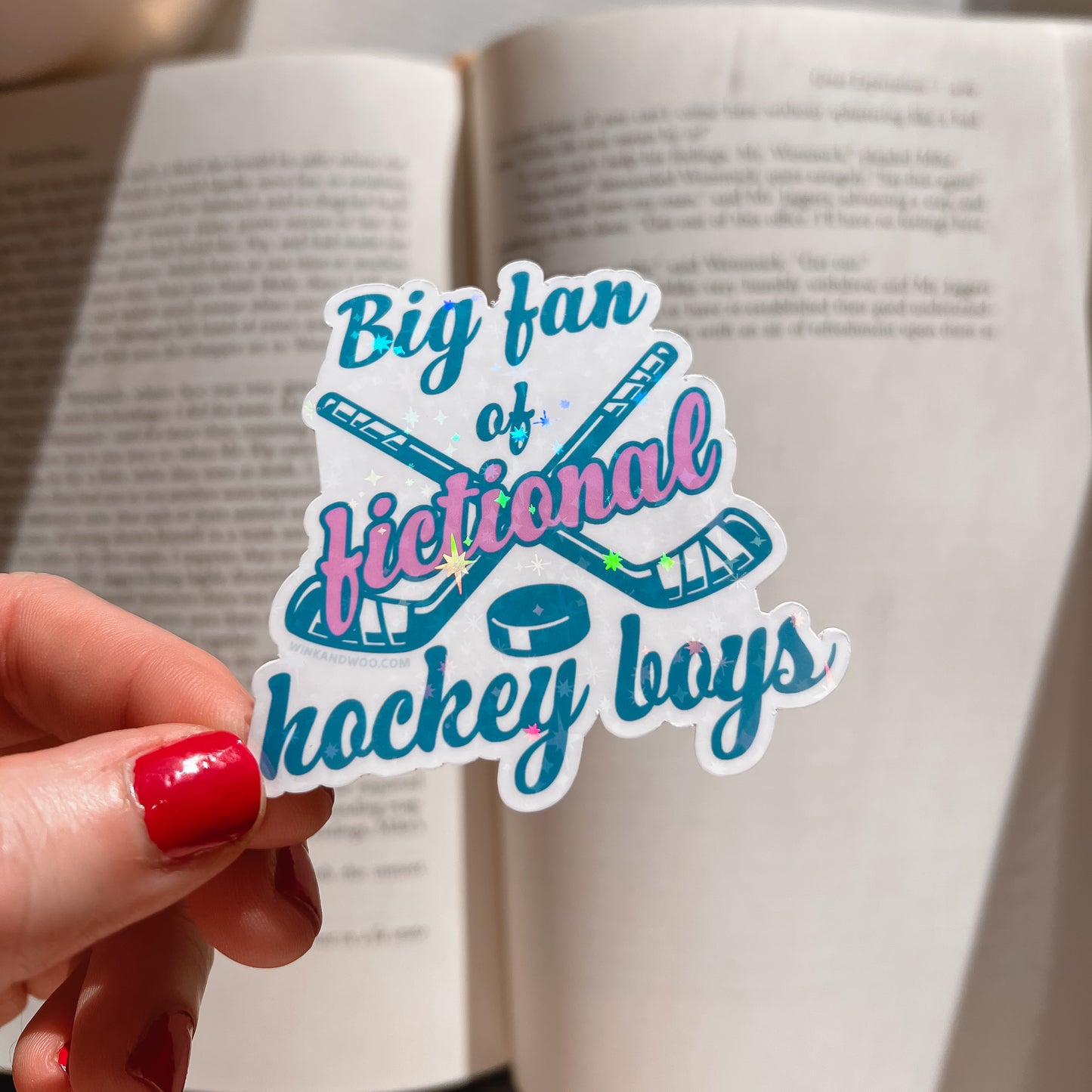 Sticker with 'Big fan of fictional hockey boys' text held over an open book.