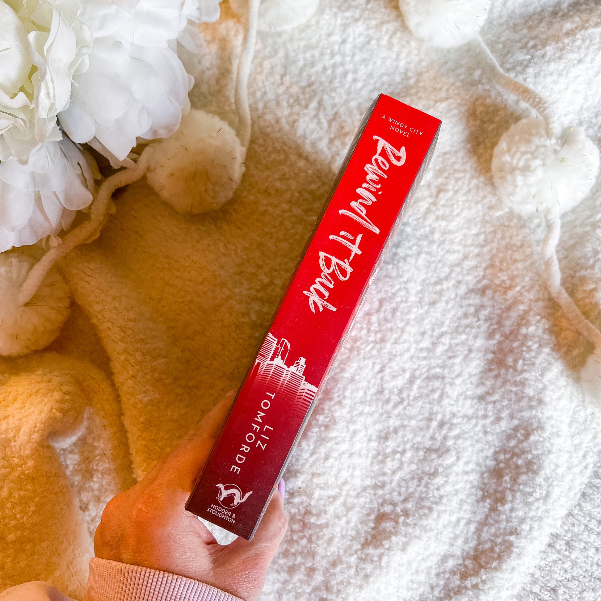 Spine of "rewind it back" held by a hand with white flowers and beige fabric in the background