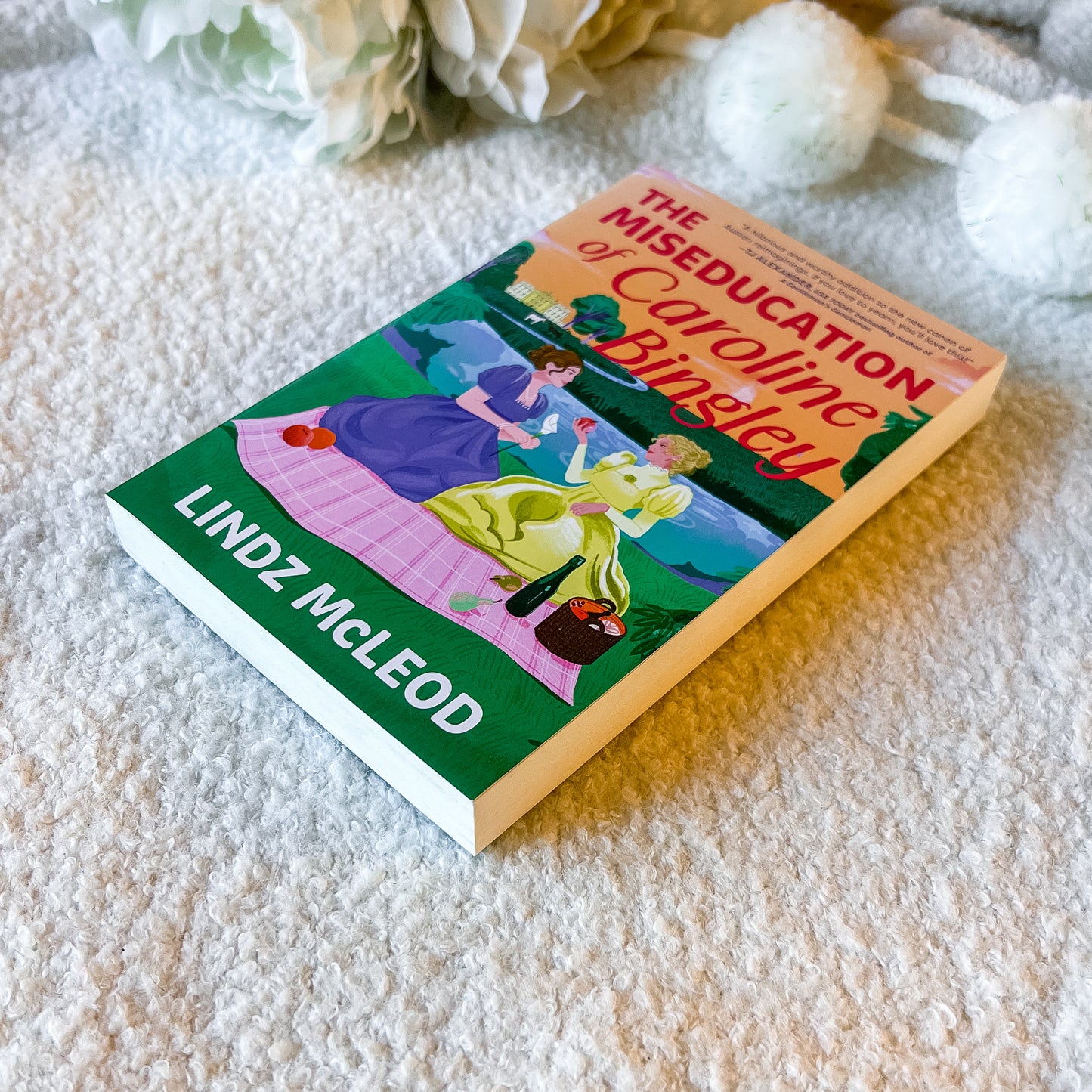 Book titled 'The Miseducation of Caroline Bingley' by Lindz McLeod on a textured surface with flowers in the background.
