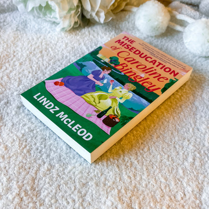 Book titled 'The Miseducation of Caroline Bingley' by Lindz McLeod on a textured surface with flowers in the background.