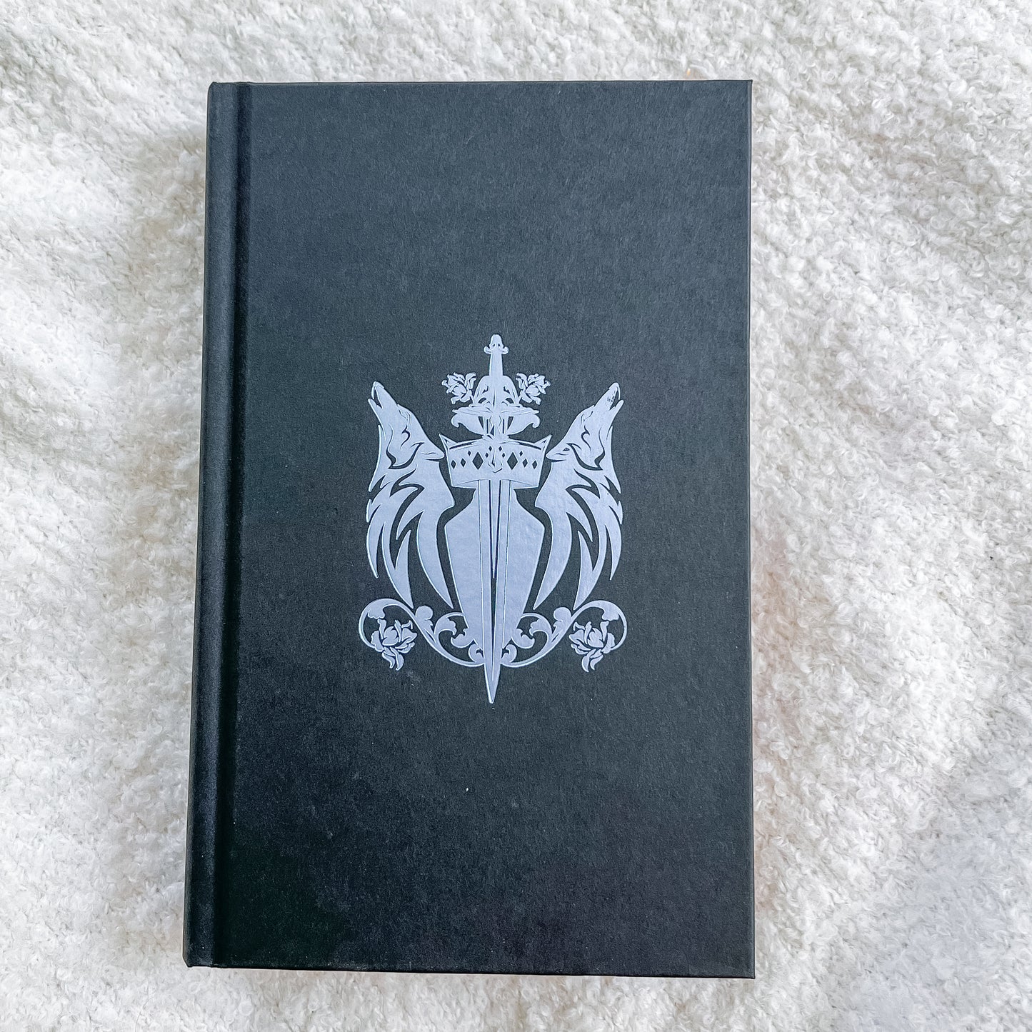 Black book with a silver emblem on a textured white surface