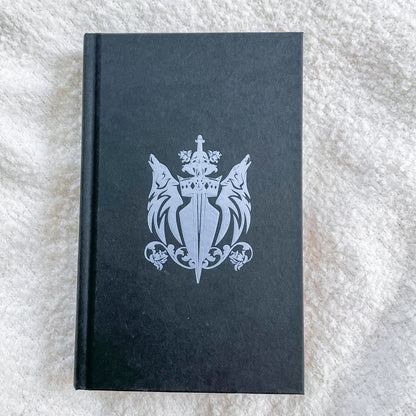 Black book with a silver emblem on a textured white surface