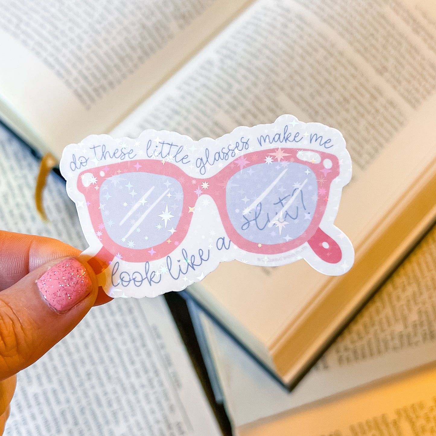 Sticker of pink sunglasses with text held by a hand over books